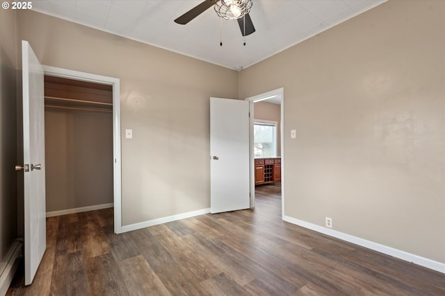 unfurnished bedroom featuring a baseboard heating unit, a closet, baseboards, and wood finished floors