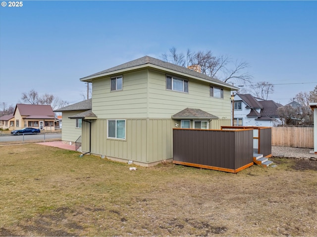 rear view of house with board and batten siding, a lawn, and fence