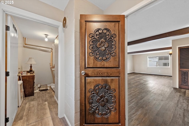 hallway featuring beamed ceiling, baseboards, and wood finished floors