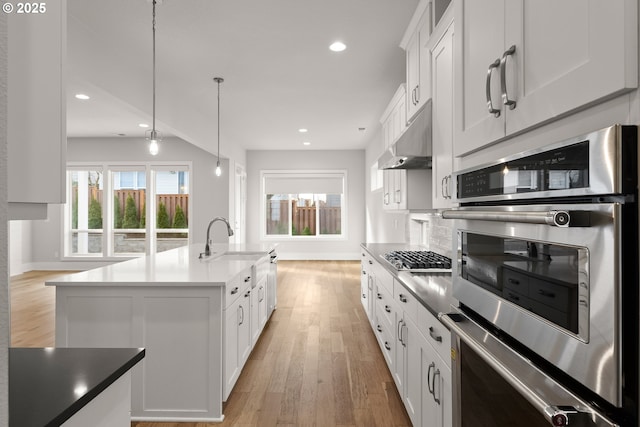 kitchen featuring sink, appliances with stainless steel finishes, white cabinetry, a center island with sink, and decorative light fixtures