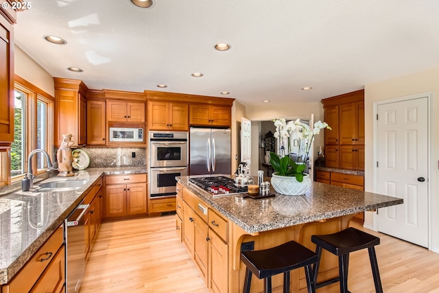 9122 NW Wood Rose Loop, Portland, OR 97229 - kitchen with appliances with stainless steel finishes, a sink, light wood finished floors, a kitchen island, and a kitchen bar