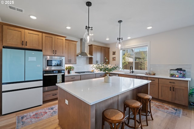 kitchen featuring appliances with stainless steel finishes, a sink, wall chimney exhaust hood, light wood-type flooring, and visible vents