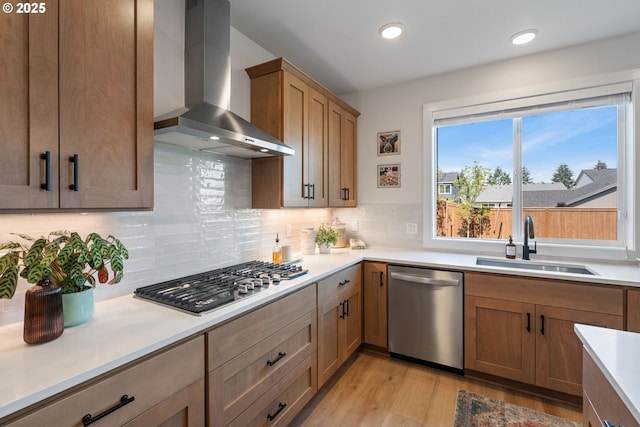 kitchen featuring light wood-style floors, wall chimney range hood, light countertops, a sink, and appliances with stainless steel finishes