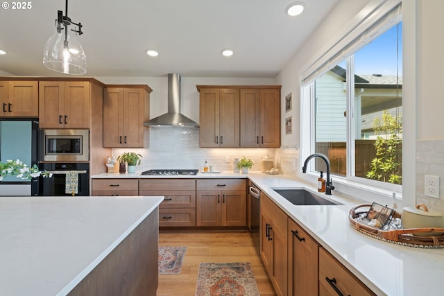kitchen with wall chimney range hood, a sink, light countertops, light wood-style flooring, and stainless steel appliances