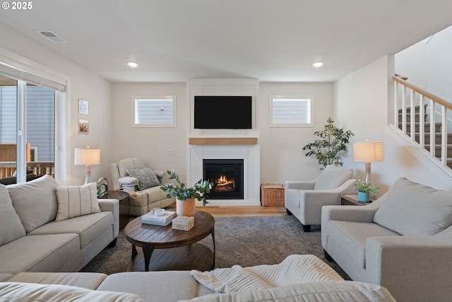 living room with visible vents, plenty of natural light, a glass covered fireplace, and wood finished floors