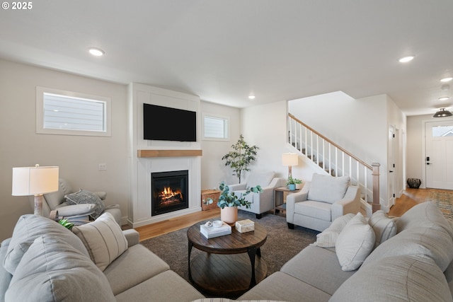 living area featuring a large fireplace, wood finished floors, stairway, baseboards, and recessed lighting