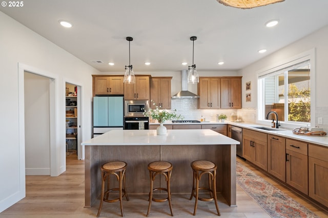 kitchen with wall chimney range hood, decorative backsplash, appliances with stainless steel finishes, a center island, and a sink