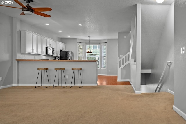 kitchen featuring white cabinets, a kitchen breakfast bar, a peninsula, hanging light fixtures, and black appliances