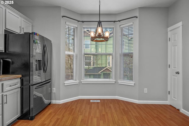 kitchen with baseboards, visible vents, decorative light fixtures, light wood-style floors, and black fridge