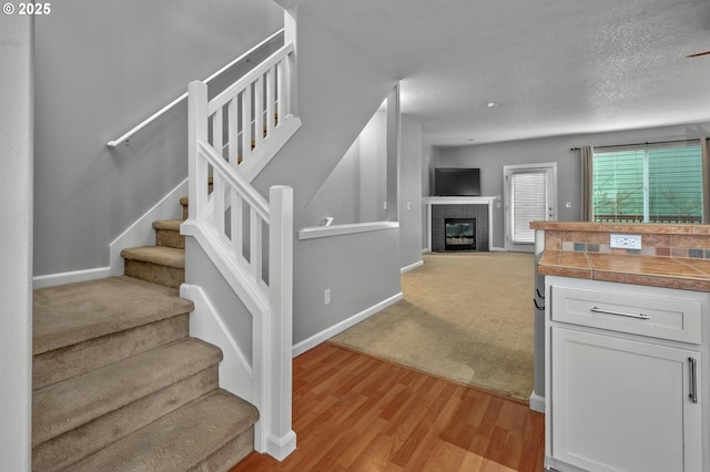 interior space featuring baseboards, a tile fireplace, open floor plan, light wood-type flooring, and white cabinetry