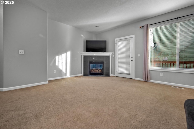 unfurnished living room with a tile fireplace, light colored carpet, visible vents, and a textured ceiling