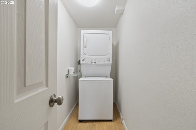 clothes washing area featuring laundry area, light wood-style flooring, baseboards, and stacked washer and dryer