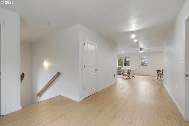 interior space with an upstairs landing, light wood-style flooring, a textured ceiling, and baseboards