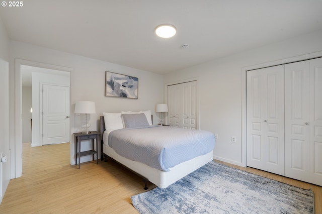 bedroom featuring two closets, light wood-type flooring, and baseboards