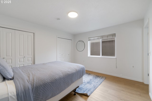 bedroom featuring wood finished floors, multiple closets, and baseboards