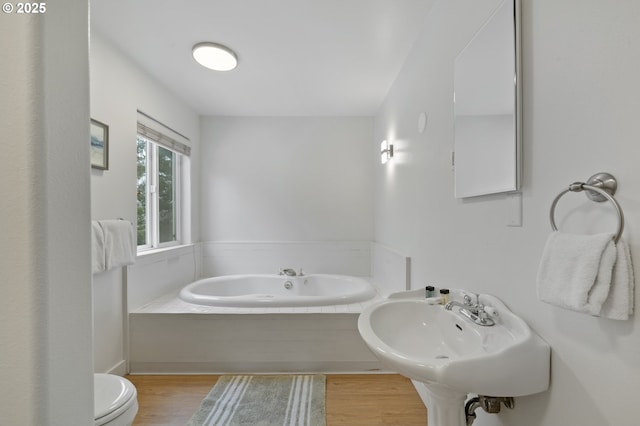 full bath featuring a bath, a sink, toilet, and wood finished floors