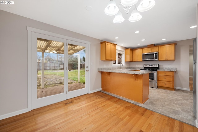 kitchen with a breakfast bar area, an inviting chandelier, appliances with stainless steel finishes, kitchen peninsula, and light hardwood / wood-style floors