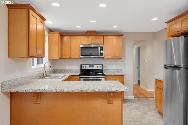 kitchen with light stone countertops, appliances with stainless steel finishes, sink, and a breakfast bar area