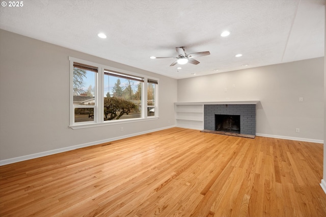 unfurnished living room with a brick fireplace, light hardwood / wood-style flooring, a textured ceiling, and ceiling fan