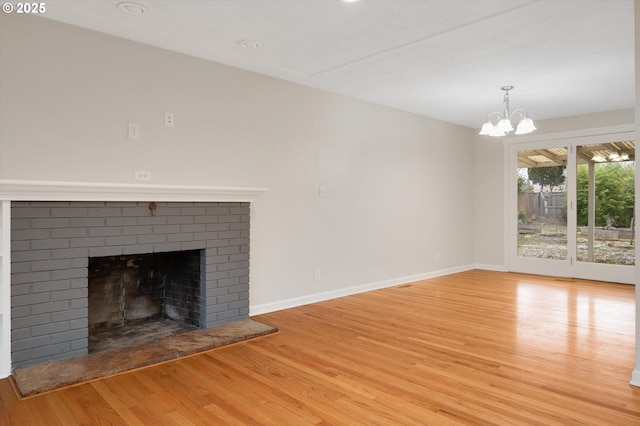 unfurnished living room with an inviting chandelier, a fireplace, and light hardwood / wood-style floors