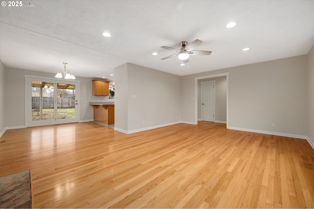 unfurnished living room featuring ceiling fan with notable chandelier, light hardwood / wood-style flooring, and a textured ceiling