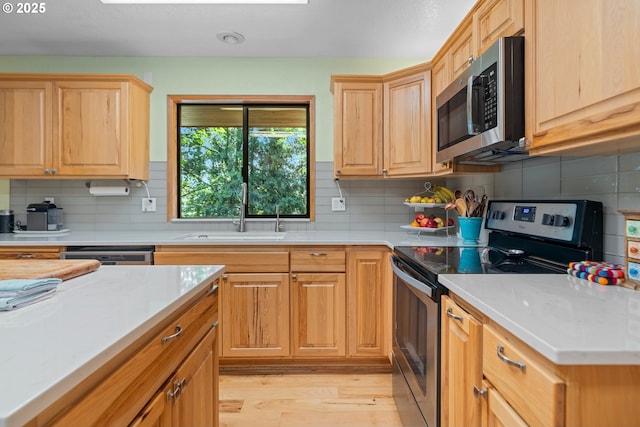 kitchen with appliances with stainless steel finishes, a sink, light wood-type flooring, decorative backsplash, and light countertops