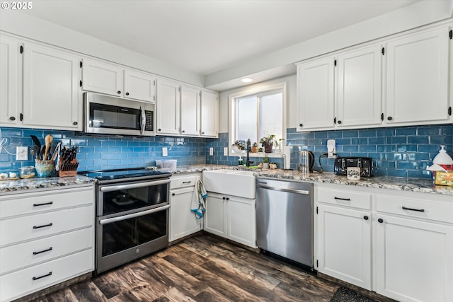 kitchen featuring appliances with stainless steel finishes, dark hardwood / wood-style floors, white cabinetry, decorative backsplash, and light stone counters