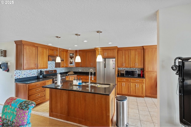 94020 E Shore Dr, North Bend, OR 97459 - kitchen with stainless steel appliances, a sink, dark countertops, brown cabinetry, and light tile patterned floors