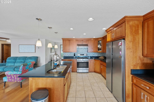 94020 E Shore Dr, North Bend, OR 97459 - kitchen featuring stainless steel appliances, dark countertops, brown cabinets, a sink, and under cabinet range hood