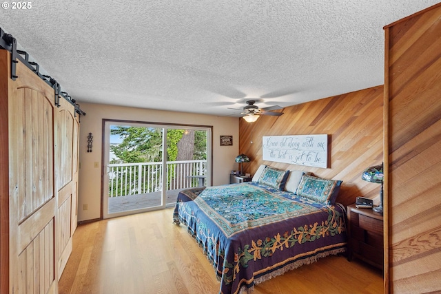 94020 E Shore Dr, North Bend, OR 97459 - bedroom featuring access to outside, light wood finished floors, a barn door, wood walls, and a textured ceiling