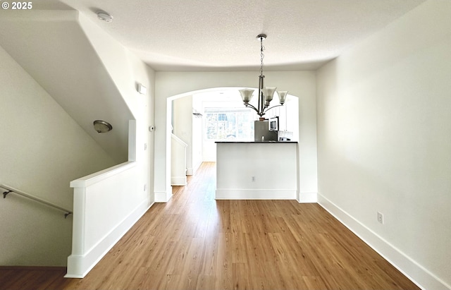 836 NW 118th Ave Unit 104, Portland, OR 97229 - unfurnished dining area with wood finished floors, baseboards, a textured ceiling, a chandelier, and arched walkways
