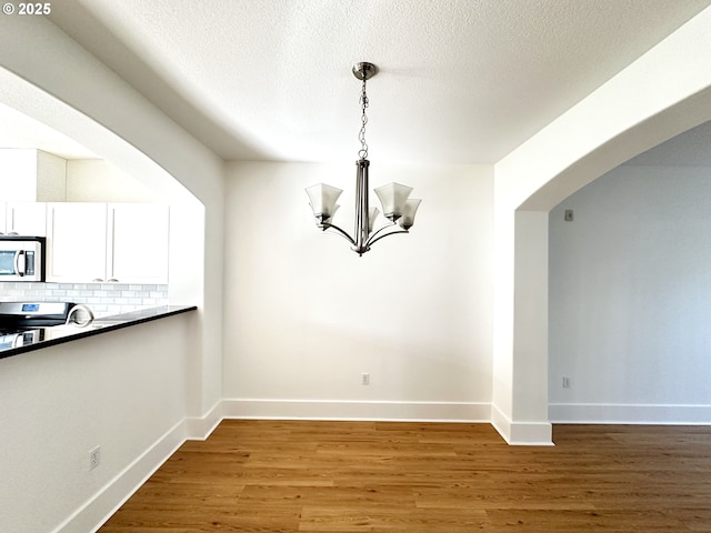 836 NW 118th Ave Unit 104, Portland, OR 97229 - unfurnished dining area with light wood-style floors, arched walkways, baseboards, and a notable chandelier