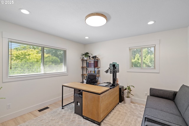 office space with visible vents, baseboards, light wood-style flooring, and a healthy amount of sunlight