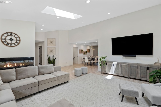 living area featuring light wood-style flooring, recessed lighting, a high ceiling, a skylight, and baseboards