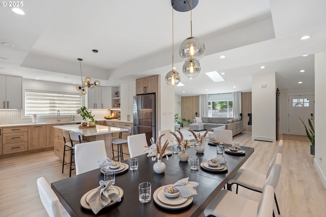 dining area with a tray ceiling, recessed lighting, a skylight, and light wood-style floors