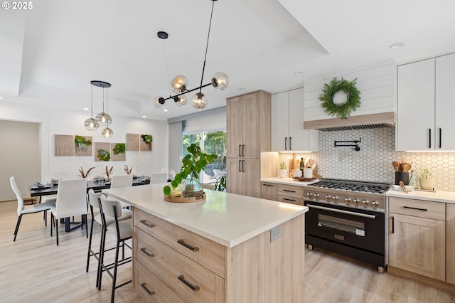 kitchen featuring tasteful backsplash, a tray ceiling, stainless steel stove, and light brown cabinets