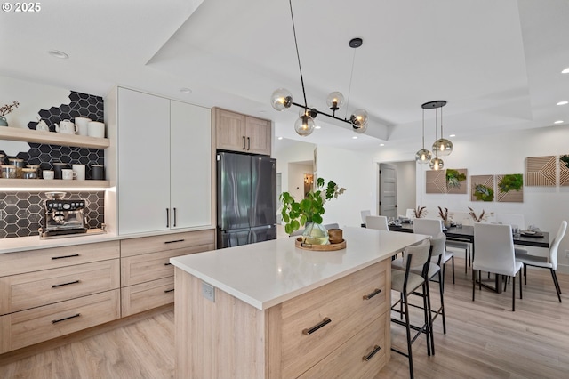 kitchen featuring light wood-style floors, a kitchen bar, light brown cabinets, and freestanding refrigerator