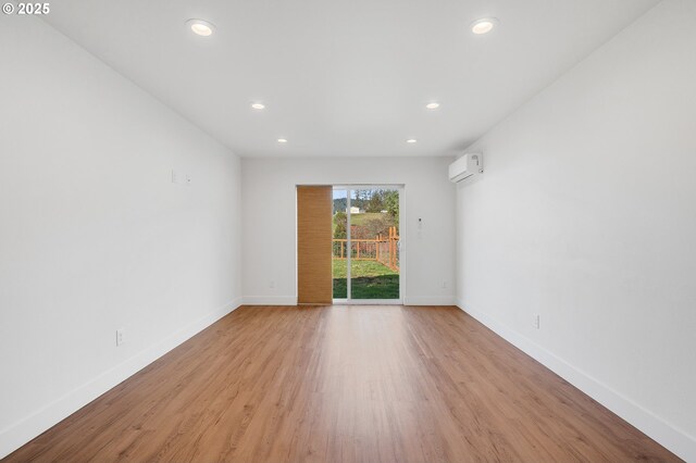 spare room featuring light wood-type flooring, a wall unit AC, baseboards, and recessed lighting