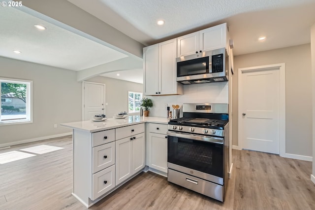 4106 SE 122nd Ave, Portland, OR 97236 - kitchen featuring appliances with stainless steel finishes, light wood-style flooring, a peninsula, arched walkways, and recessed lighting
