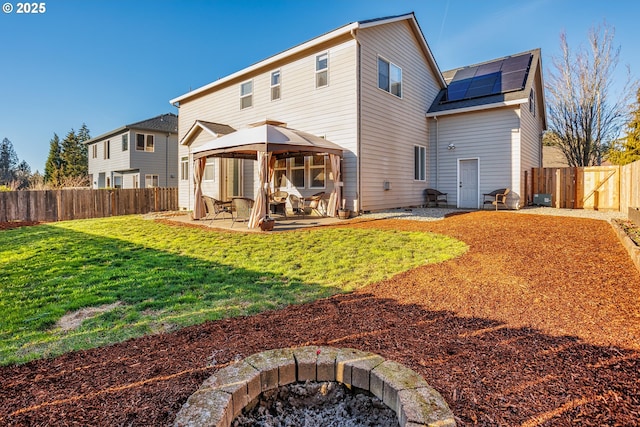 rear view of property featuring a patio, a yard, an outdoor fire pit, a gazebo, and solar panels