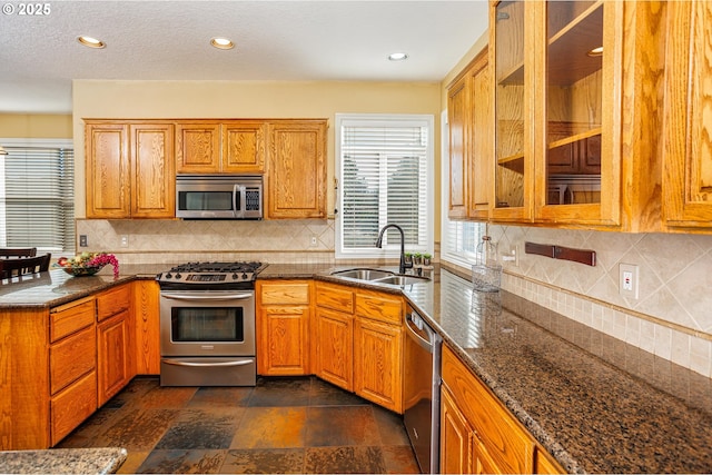 kitchen featuring appliances with stainless steel finishes, sink, decorative backsplash, and dark stone counters