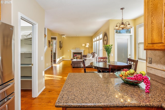 kitchen with stone countertops, pendant lighting, tasteful backsplash, stainless steel fridge, and light hardwood / wood-style floors