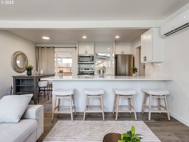 kitchen featuring stainless steel appliances, a wall mounted AC, white cabinets, light countertops, and a peninsula