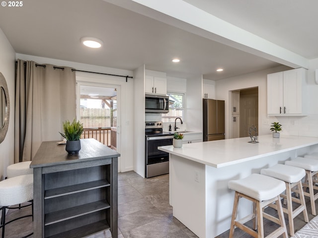 kitchen with stainless steel appliances, white cabinetry, a breakfast bar, a peninsula, and decorative backsplash