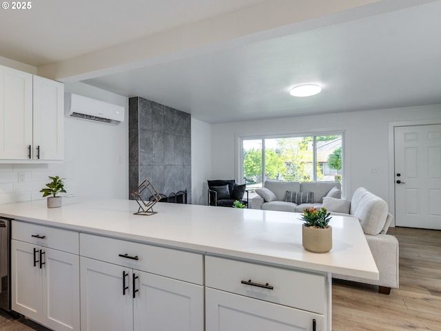 kitchen featuring an AC wall unit, open floor plan, white cabinetry, light countertops, and light wood-type flooring