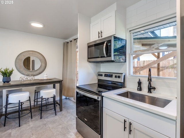 kitchen with appliances with stainless steel finishes, a sink, white cabinets, light countertops, and backsplash