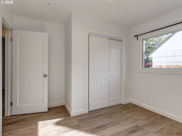 unfurnished bedroom with baseboards, light wood finished floors, and a closet