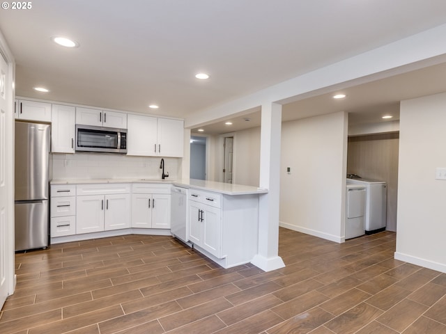 kitchen with appliances with stainless steel finishes, a sink, washer and dryer, light countertops, and baseboards