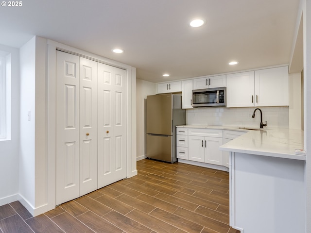 kitchen featuring stainless steel appliances, a sink, dark wood finished floors, baseboards, and white cabinets