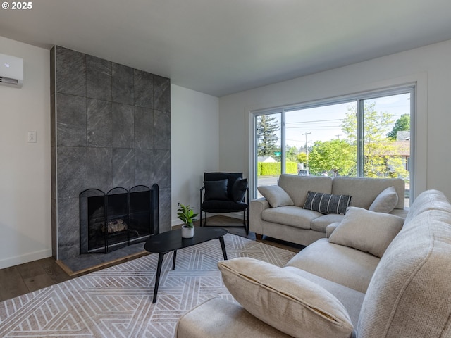 living room with a wall mounted AC, wood finished floors, a tile fireplace, and baseboards